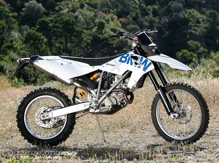 a white dirt bike parked on top of a dry grass field in front of trees