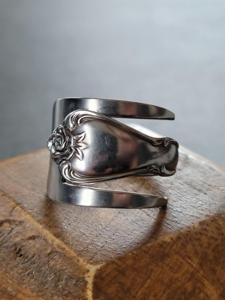 a close up of a silver ring on top of a wooden block with a metal object in the background