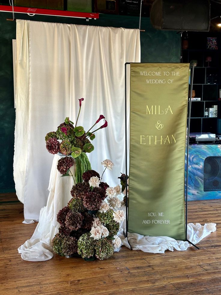 a tall vase filled with flowers sitting next to a banner on top of a wooden floor