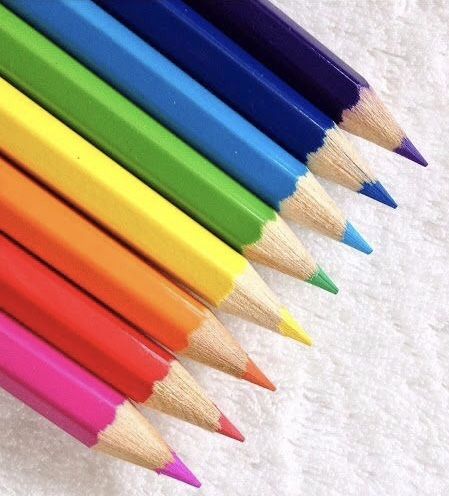 several colored pencils lined up in a row on a white sheeted surface,