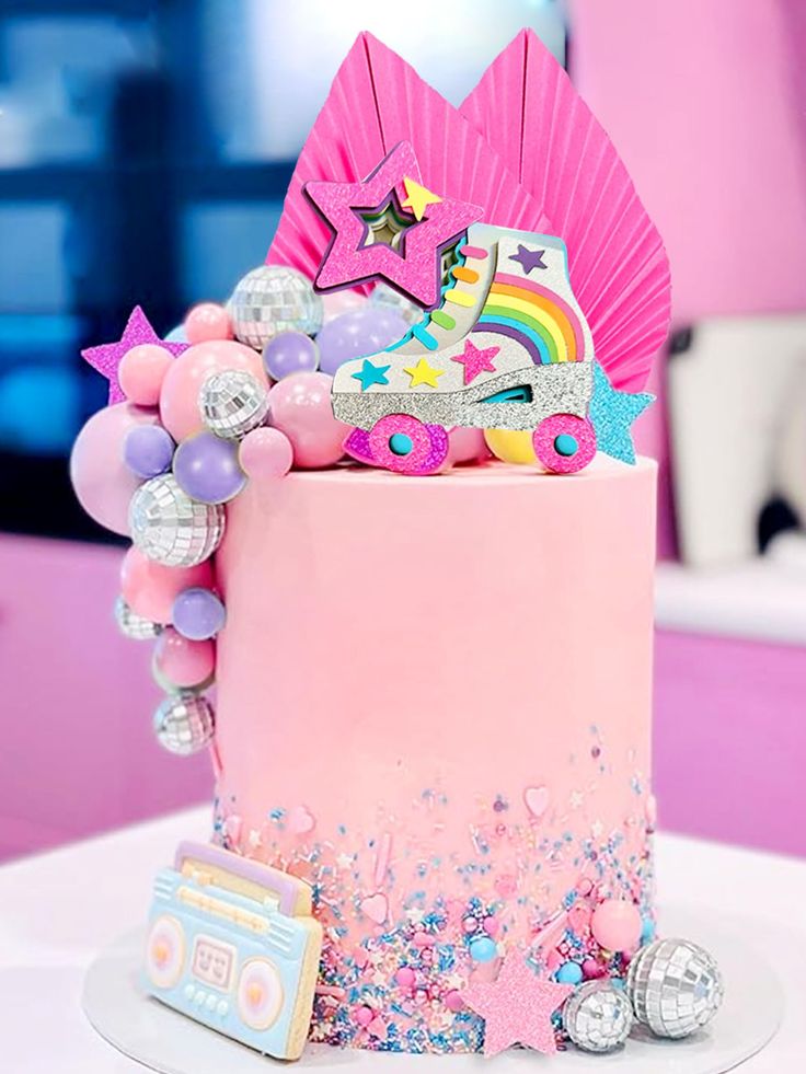 a pink birthday cake decorated with stars, balloons and confetti on a table