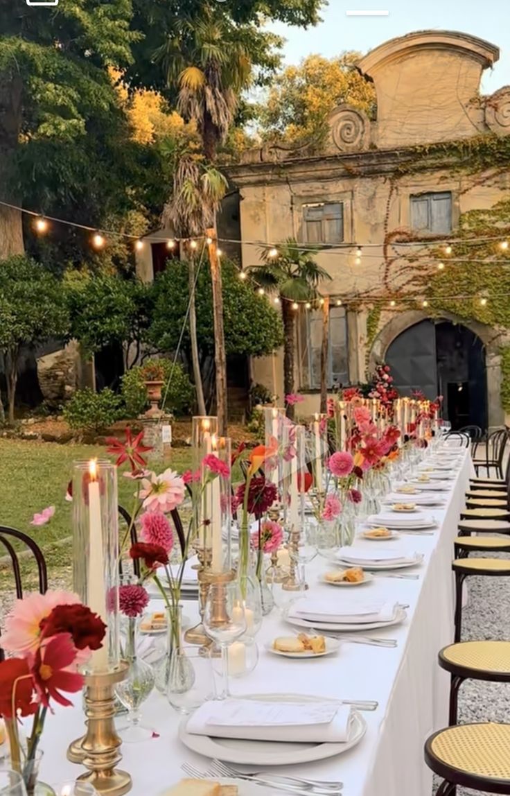 a long table is set up with flowers and candles for an outdoor dinner in the garden