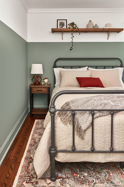 a bedroom with green walls and a metal bed frame in the middle, along with a rug on the floor