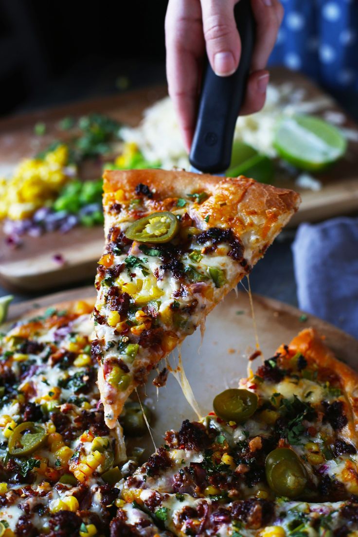 a person taking a slice of pizza from a wooden platter with several different toppings