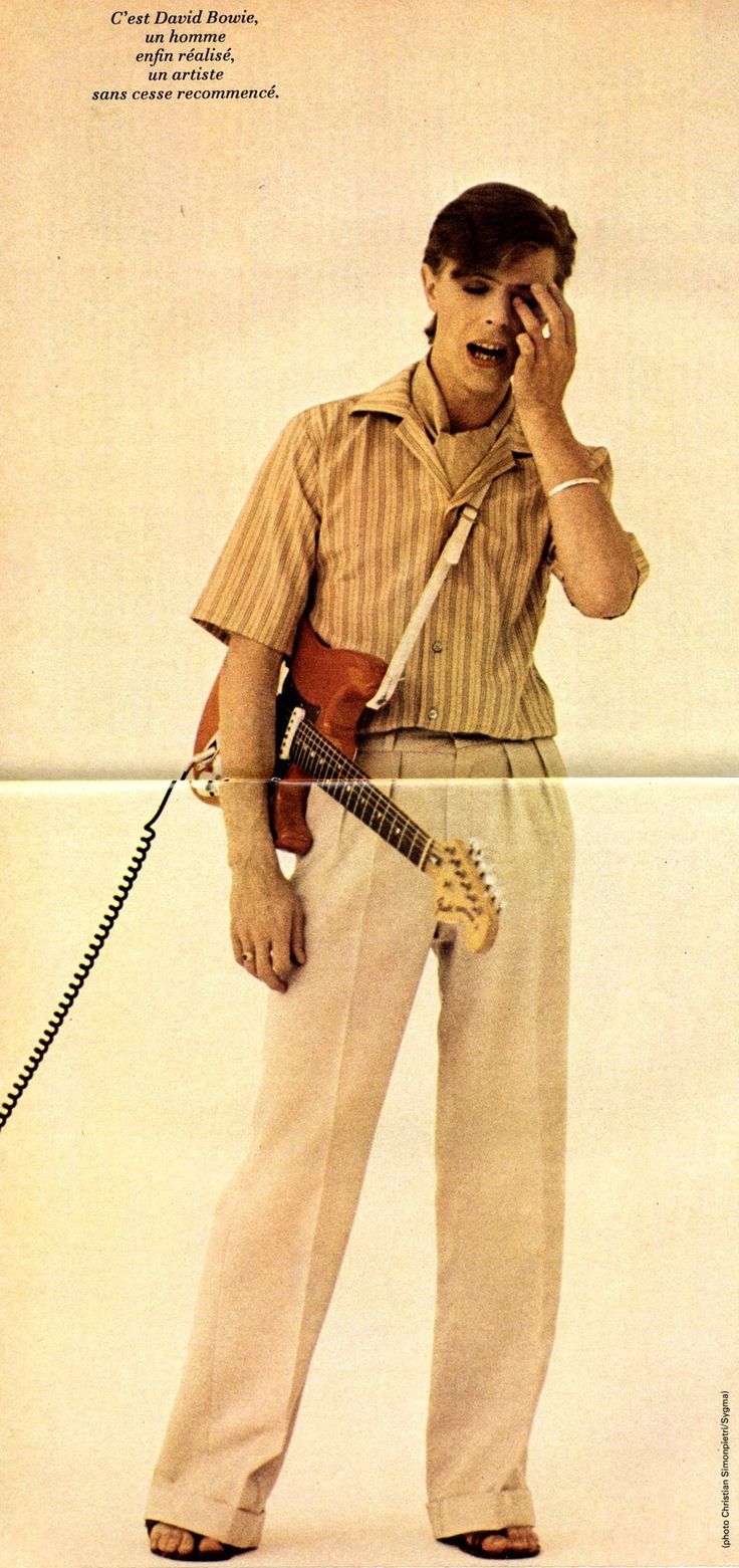 a man holding a guitar and talking on a cell phone while standing in front of a white background