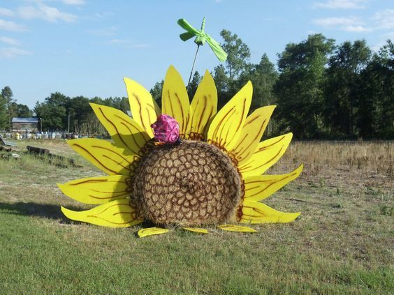 a large sunflower sculpture in the middle of a field with a pink flower on it's head