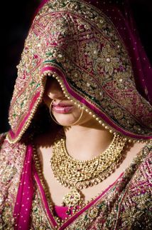 a woman in a red and gold bridal outfit with jewelry on her head, looking down at the ground