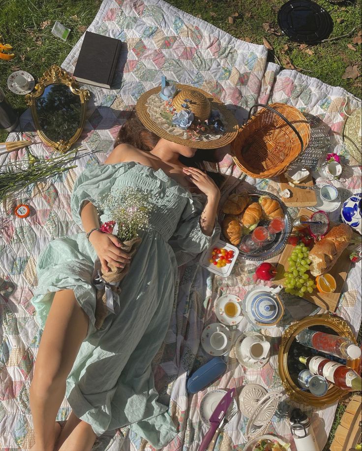 a woman laying on top of a blanket covered in food and drinks next to a basket