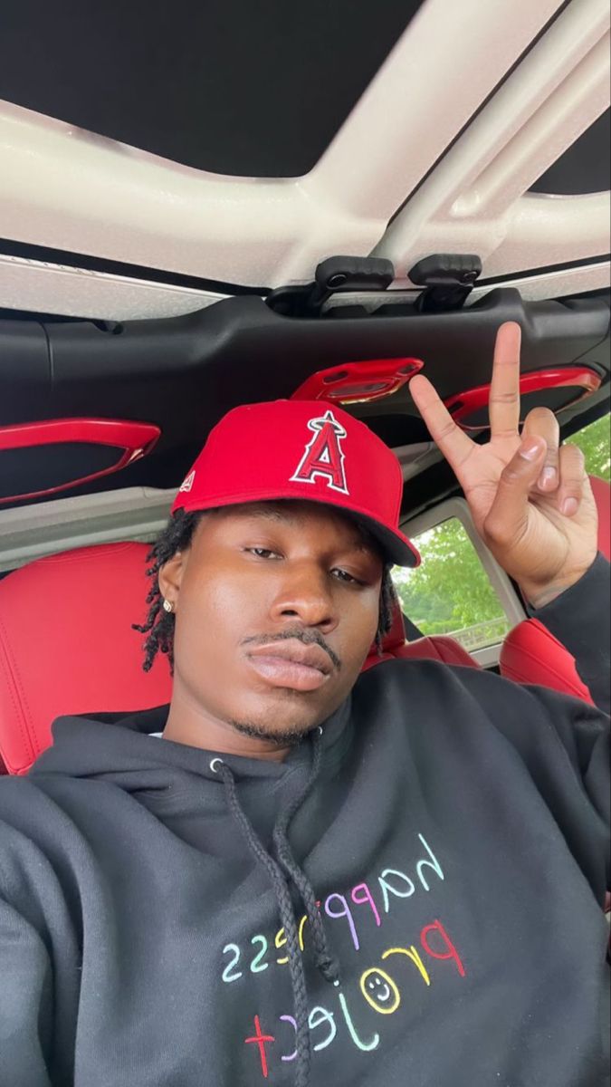 a man sitting in the back seat of a car wearing a red hat and holding up his peace sign