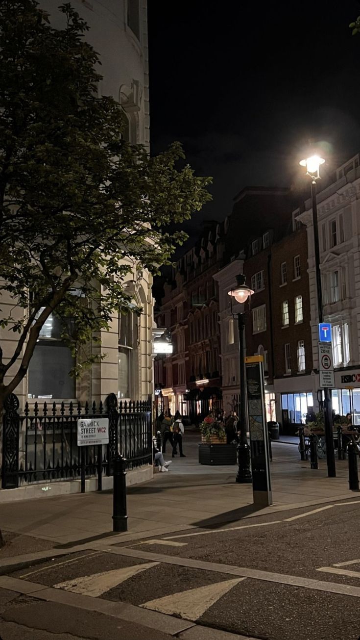 an empty city street at night with people walking on the sidewalk