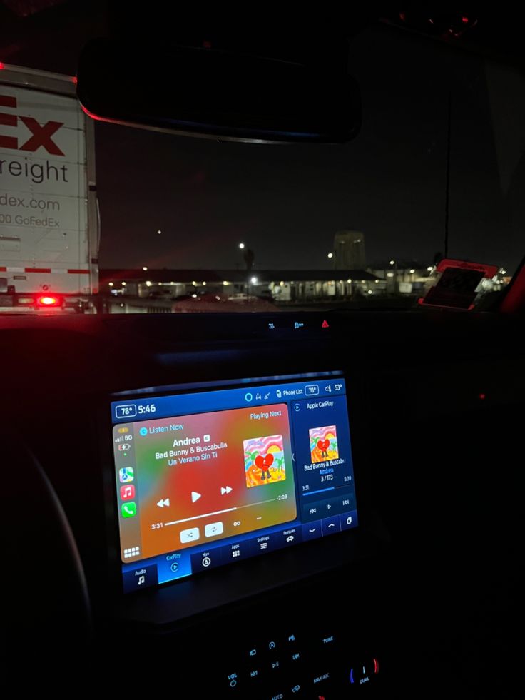 the dashboard of a vehicle at night with an ex freight truck in the background and lights on