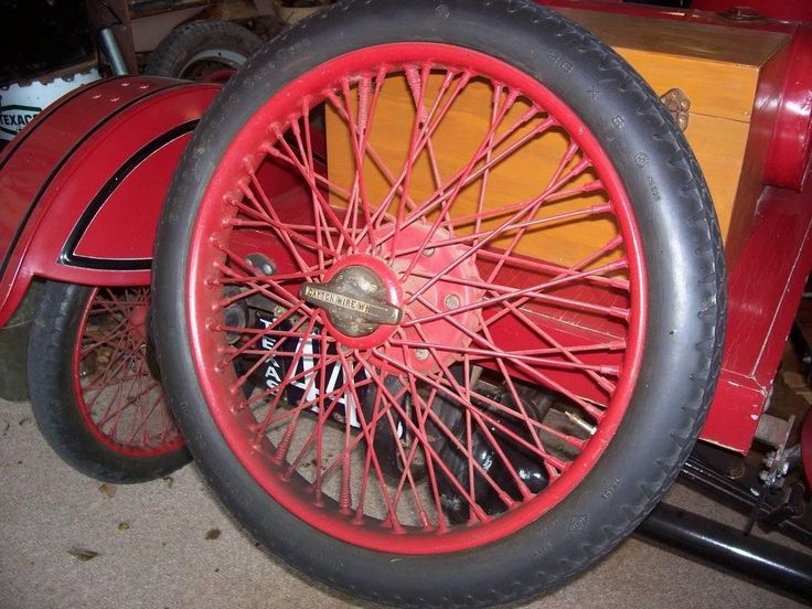 an old fashioned red car with spokes and wheels is parked in a garage next to other antique cars