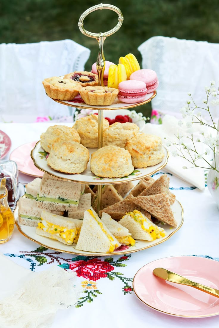 a three tiered tray filled with sandwiches and pastries on top of a table