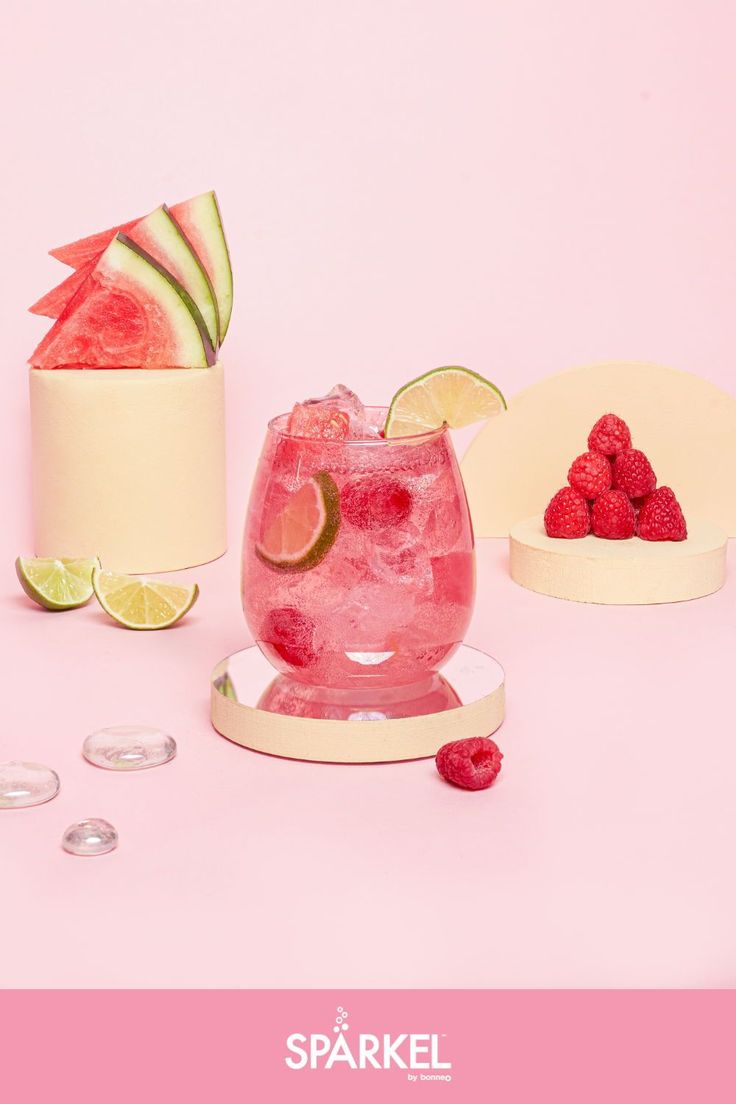 a pink drink with raspberries and limes on the rim next to it