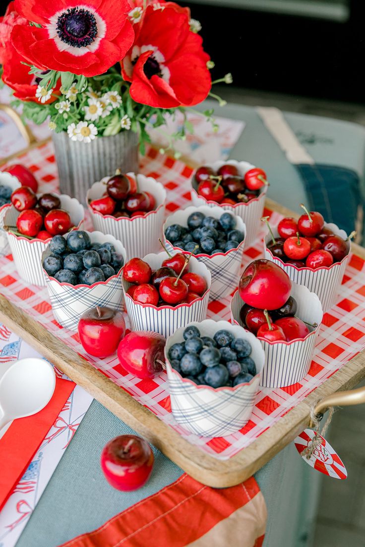 an arrangement of cherries, blueberries and apples on a table with red flowers