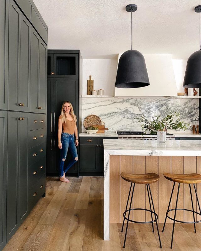 a woman standing in a kitchen next to two bar stools and an island with marble counter tops