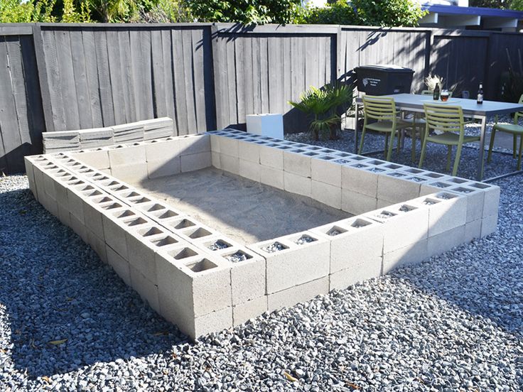 a concrete fire pit sitting in the middle of a gravel covered yard with tables and chairs around it