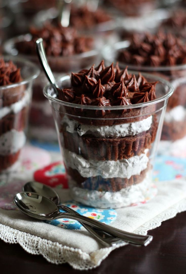 chocolate cupcakes with whipped cream and sprinkles in plastic cups on a table