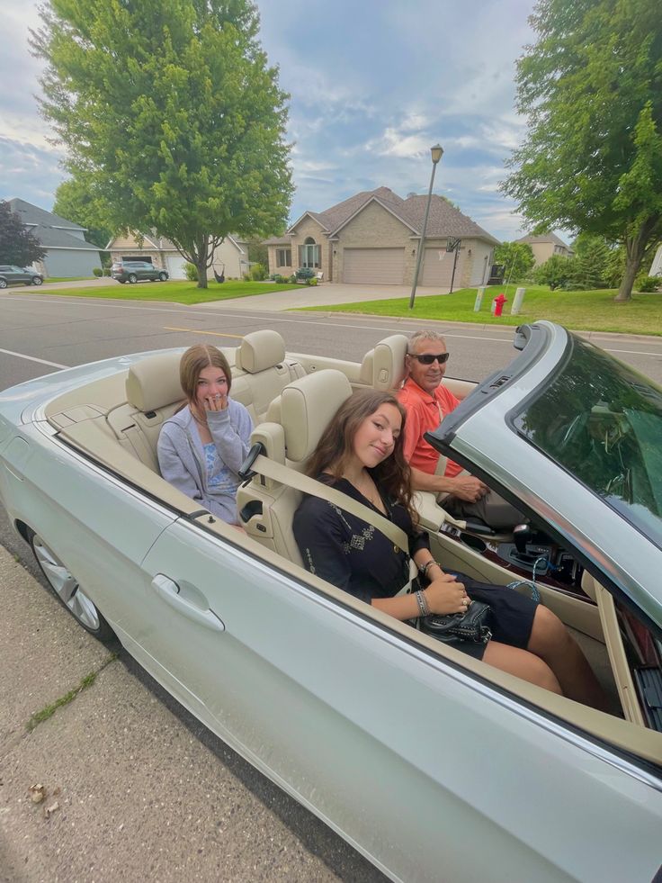 three people are sitting in the back of a convertible car, one woman is driving