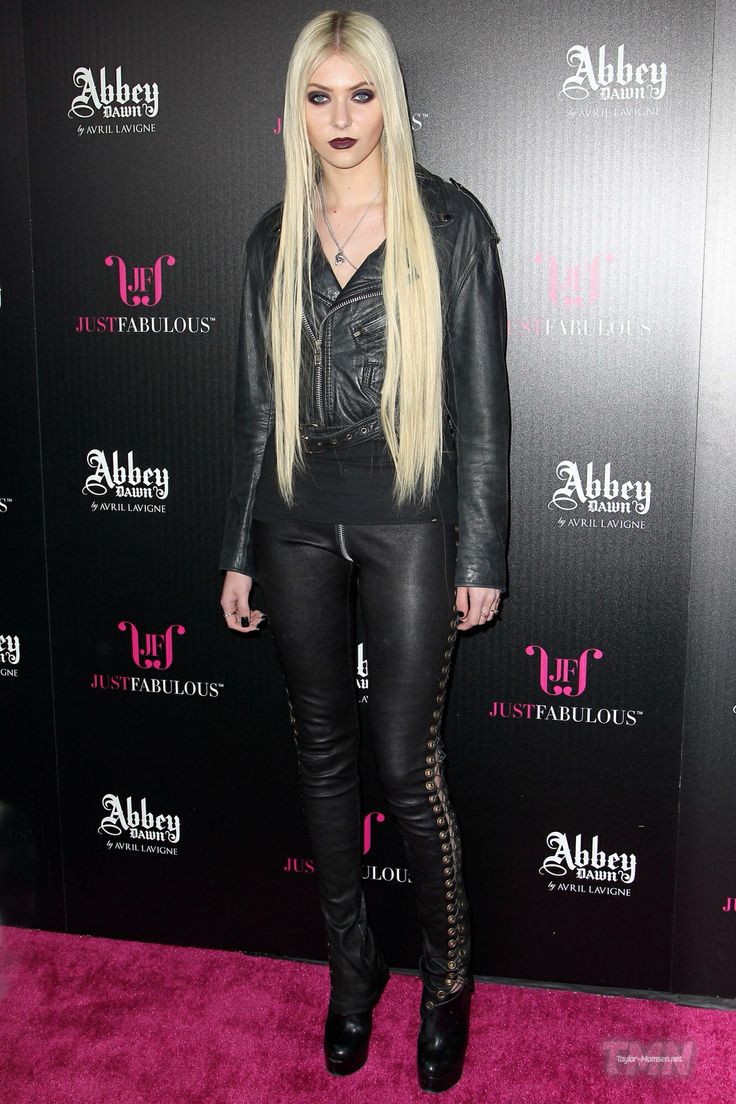 the blonde haired lady is wearing all black and posing for a photo on the pink carpet