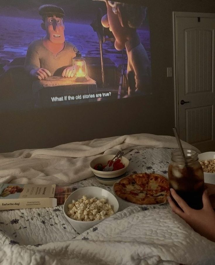 a person laying in bed watching a movie on the screen with pizza, popcorn and drinks