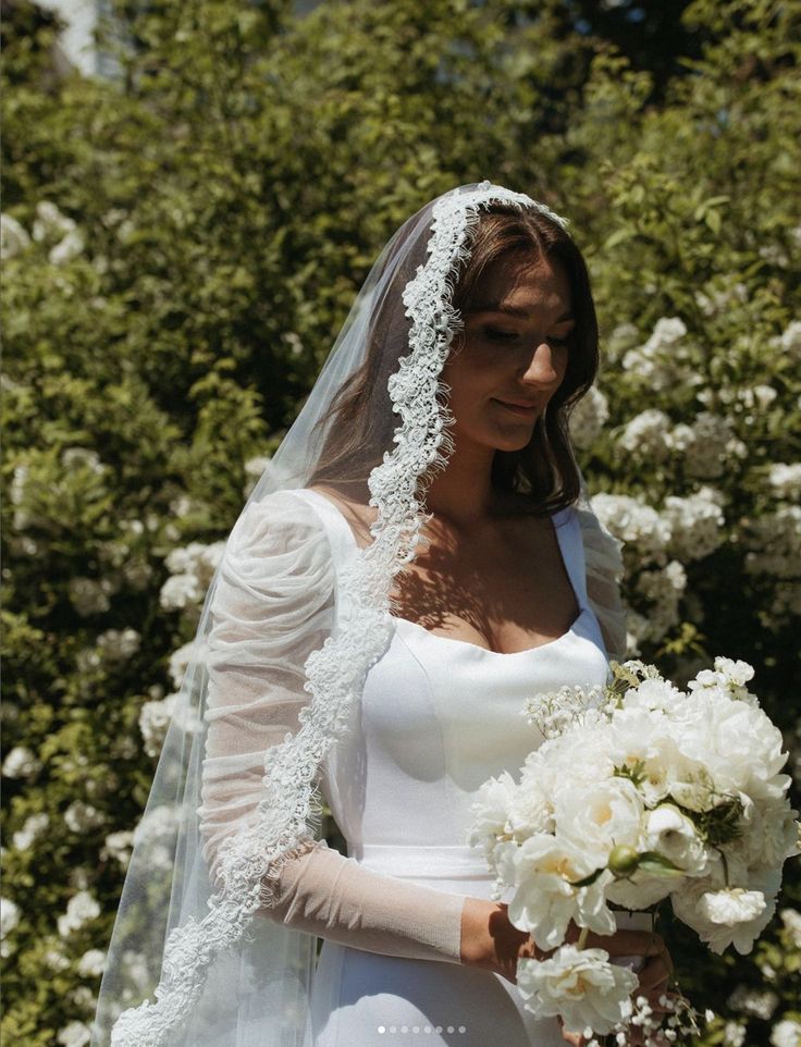 a woman in a white wedding dress holding a bouquet and wearing a veil with flowers on it