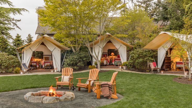 a couple of chairs sitting in front of a fire pit on top of a lush green field