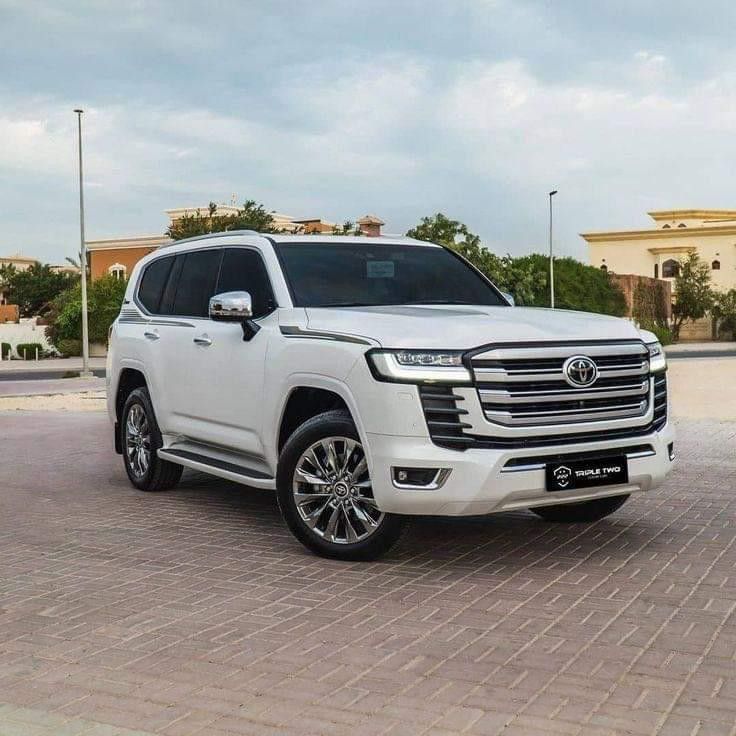 a white suv parked in front of a building on a brick road with palm trees behind it