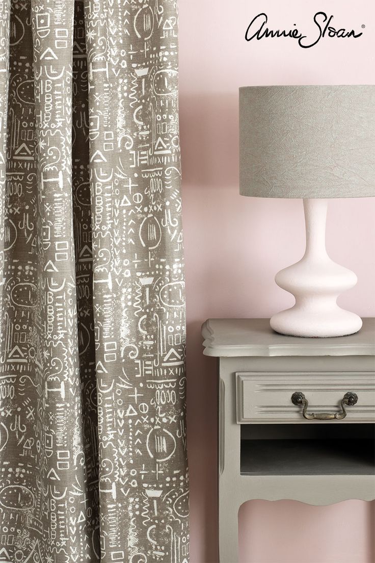 a white lamp sitting on top of a wooden table next to a window covered in curtains