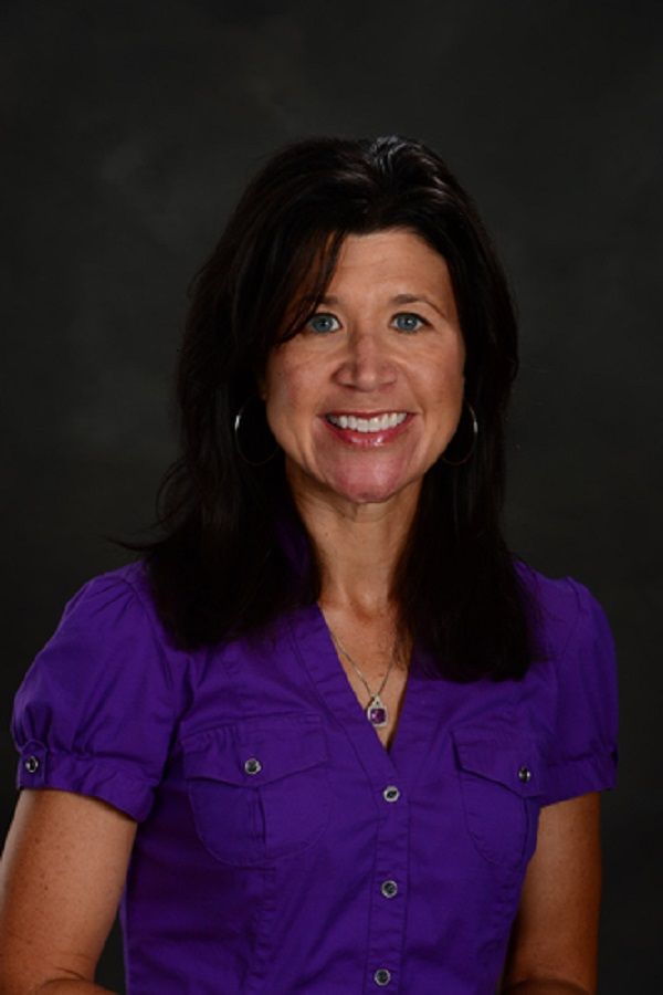 a woman in a purple shirt smiling at the camera with her hands on her hips