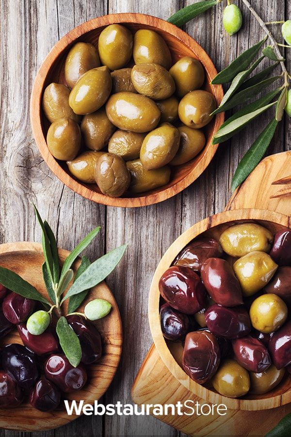 three wooden bowls filled with different types of olives and green leaves on top of a wooden table