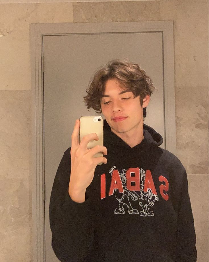 a young man taking a selfie in front of a mirror with his cell phone