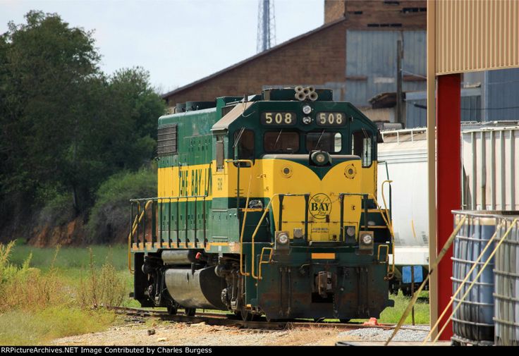 a green and yellow train is on the tracks near some buildings with trees in the background