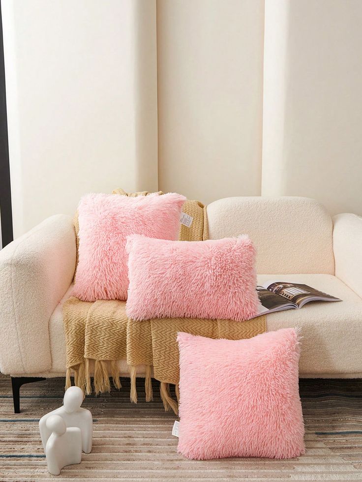 three pink pillows sitting on top of a white couch