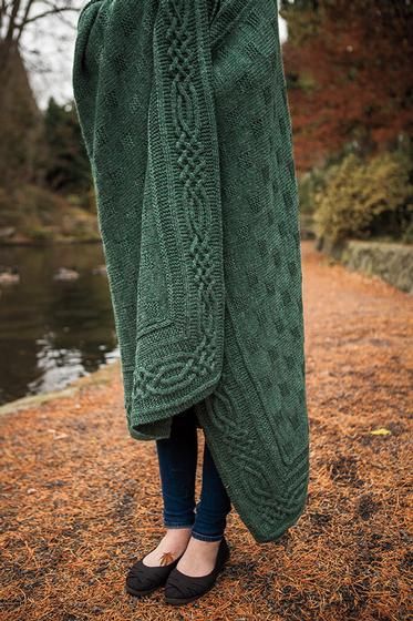 a woman is wrapped up in a green shawl by the water's edge