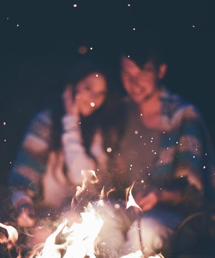 a man and woman sitting next to a campfire with sparkles in the air