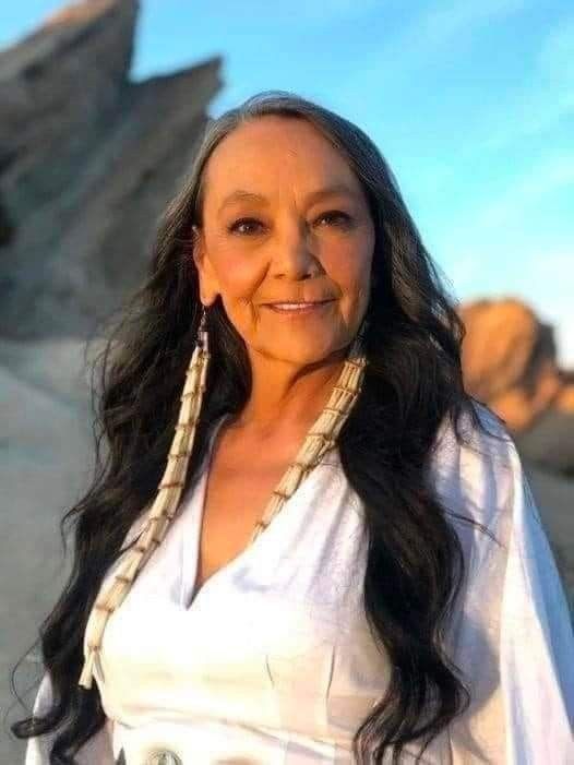 a woman with long hair and earrings standing in front of some rocks, smiling at the camera