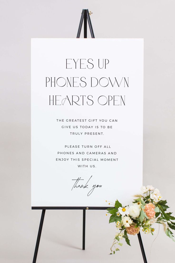 an easel with flowers on it next to a sign that says eyes up phones down hearts open