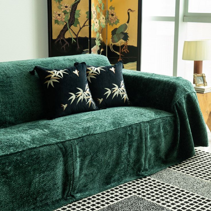 a green couch with two black and white pillows on top of it next to a lamp