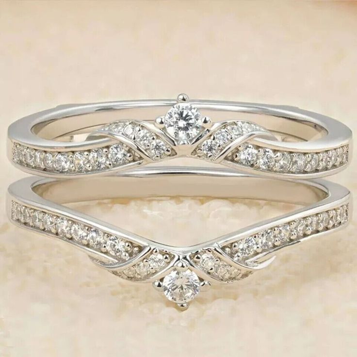 two wedding rings with diamonds on top of each other, one is white gold and the other is silver