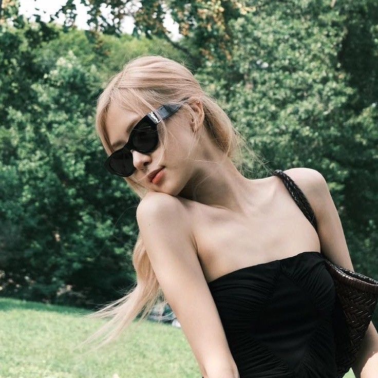 a woman with sunglasses on her head is sitting in the grass wearing a black dress