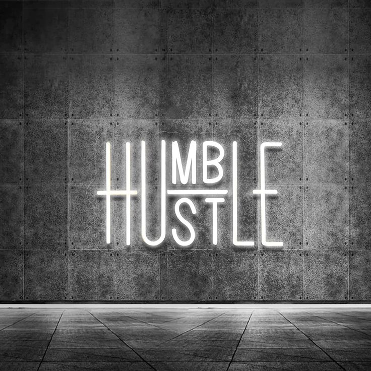 the words humble hustle are lit up in front of a concrete wall and floor