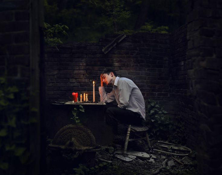 a man sitting at a table with candles in front of him and his head down