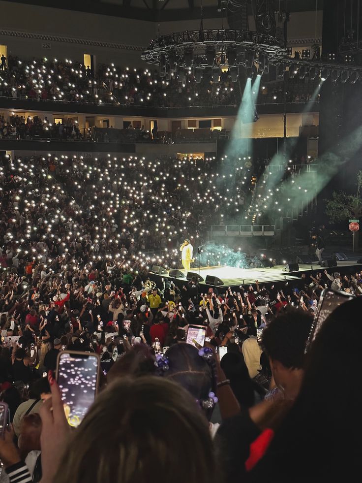 a large group of people sitting in front of a stage with lights on the ceiling