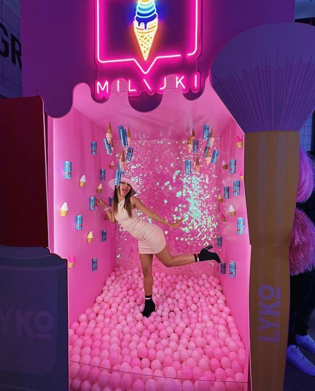 a woman posing in front of a pink ice cream parlor with balls all over the floor