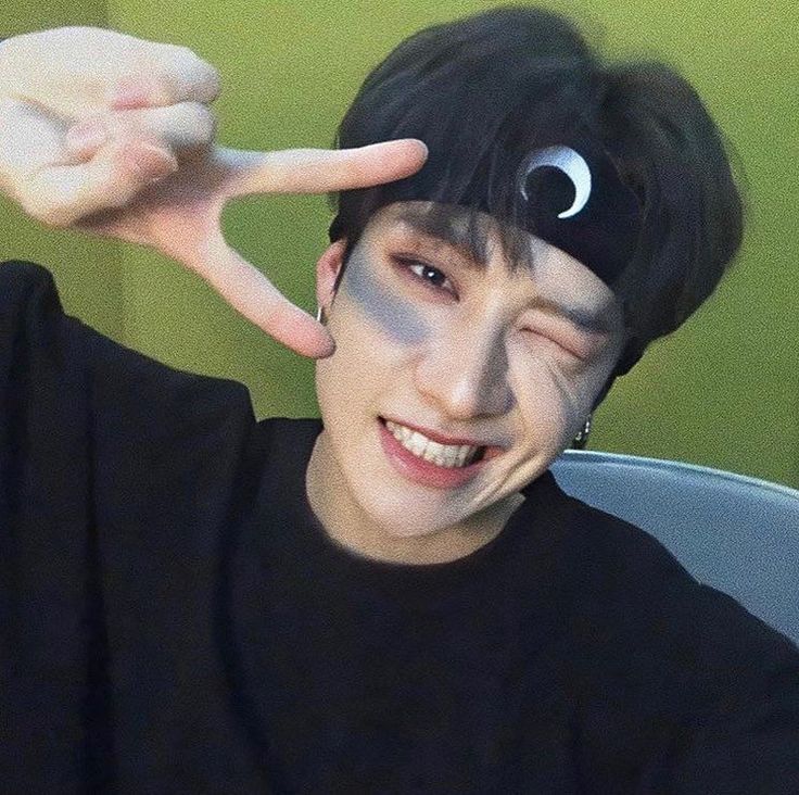 a man with black hair and fake eyes making the peace sign