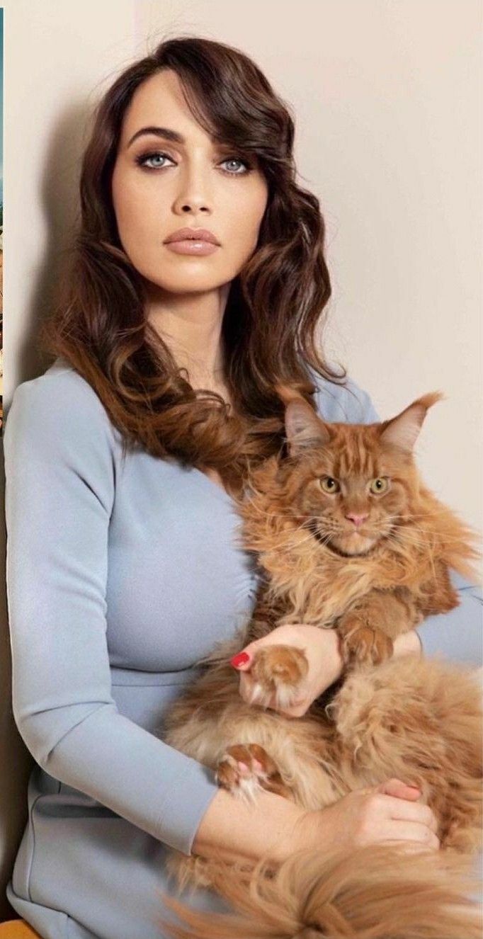 a woman holding a cat in her arms and looking at the camera with an intense look on her face