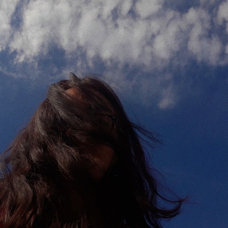 a woman is flying a kite in the sky with her long hair blowing in the wind