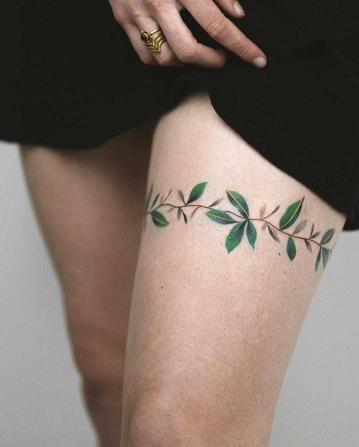 a woman's legs with green leaves on the thigh and tattoo designs on them