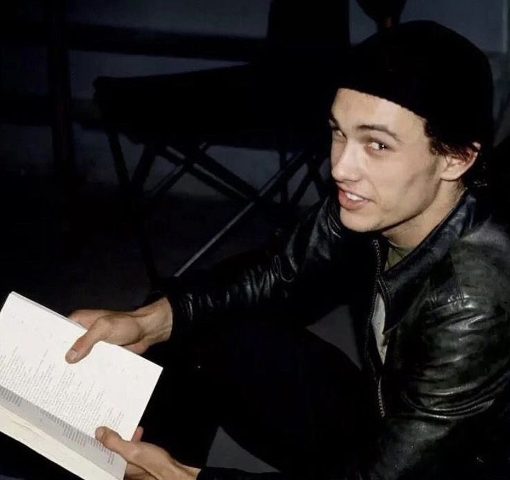 a man sitting down reading a book with his hand on top of an open book